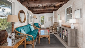A cozy room with a wooden ceiling, a teal sofa, wicker furniture, and a bookshelf. - Bayfront on Broadkill Beach! 1810 S Bayshore (Milton)