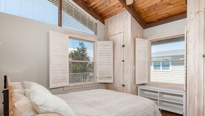 A bedroom with a large bed, wooden ceiling beams, and a view of the outdoors through open shutters. - Bayfront on Broadkill Beach! 1810 S Bayshore (Milton)