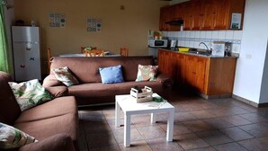 A cozy living room with a brown sofa, a white coffee table, and a kitchen area with wooden cabinets and a microwave. - Casa Oscar (Los Llanos de Aridane)