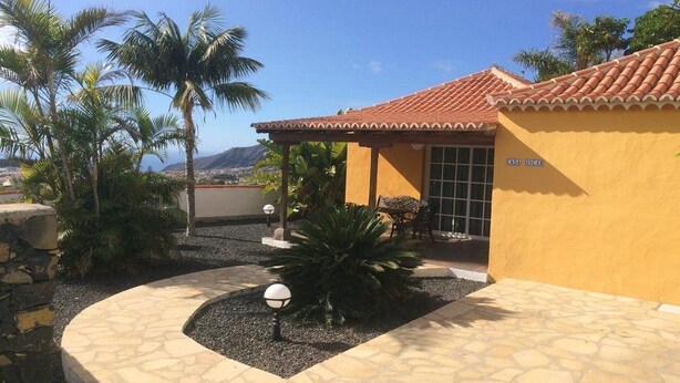 A yellow building with a tiled roof and a stone pathway leading to a covered patio area. - Casa Oscar (Los Llanos de Aridane)