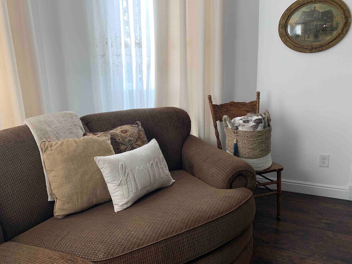 A brown sofa with patterned cushions and a small wooden chair with a basket.
