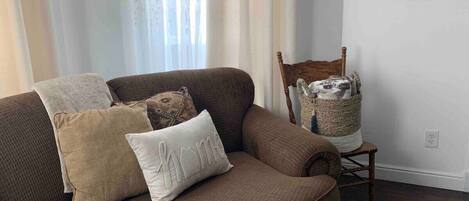 A brown sofa with patterned cushions and a small wooden chair with a basket.