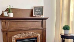 A fireplace with a stone surround, a welcome sign, a framed picture, and a small potted plant. - Jailer`s Cottage | 130-Year-Old Gem | Sleeps 12 (Spring City)