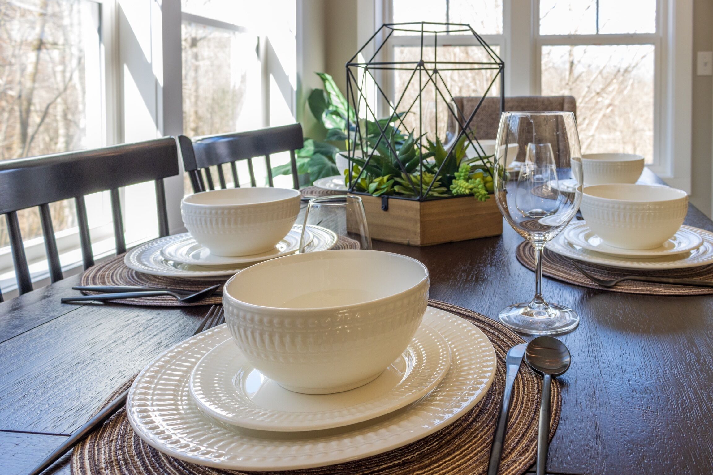 Une table à manger dressée avec des bols, des assiettes et des couverts blancs, accompagnée d’un verre et d’un chandelier en métal.
