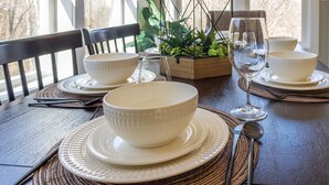 A dining table set with white bowls, plates, and cutlery, accompanied by a glass and a metal candle holder. - Hot Tub, Cozy, Central Air and Heat, 5 minutes to the Ski Resort! Yes, Deer!  (Beech Mountain)