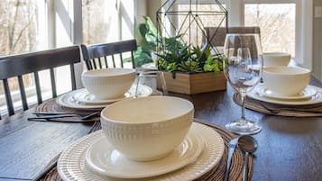A dining table set with white bowls, plates, and cutlery, accompanied by a glass and a metal candle holder.