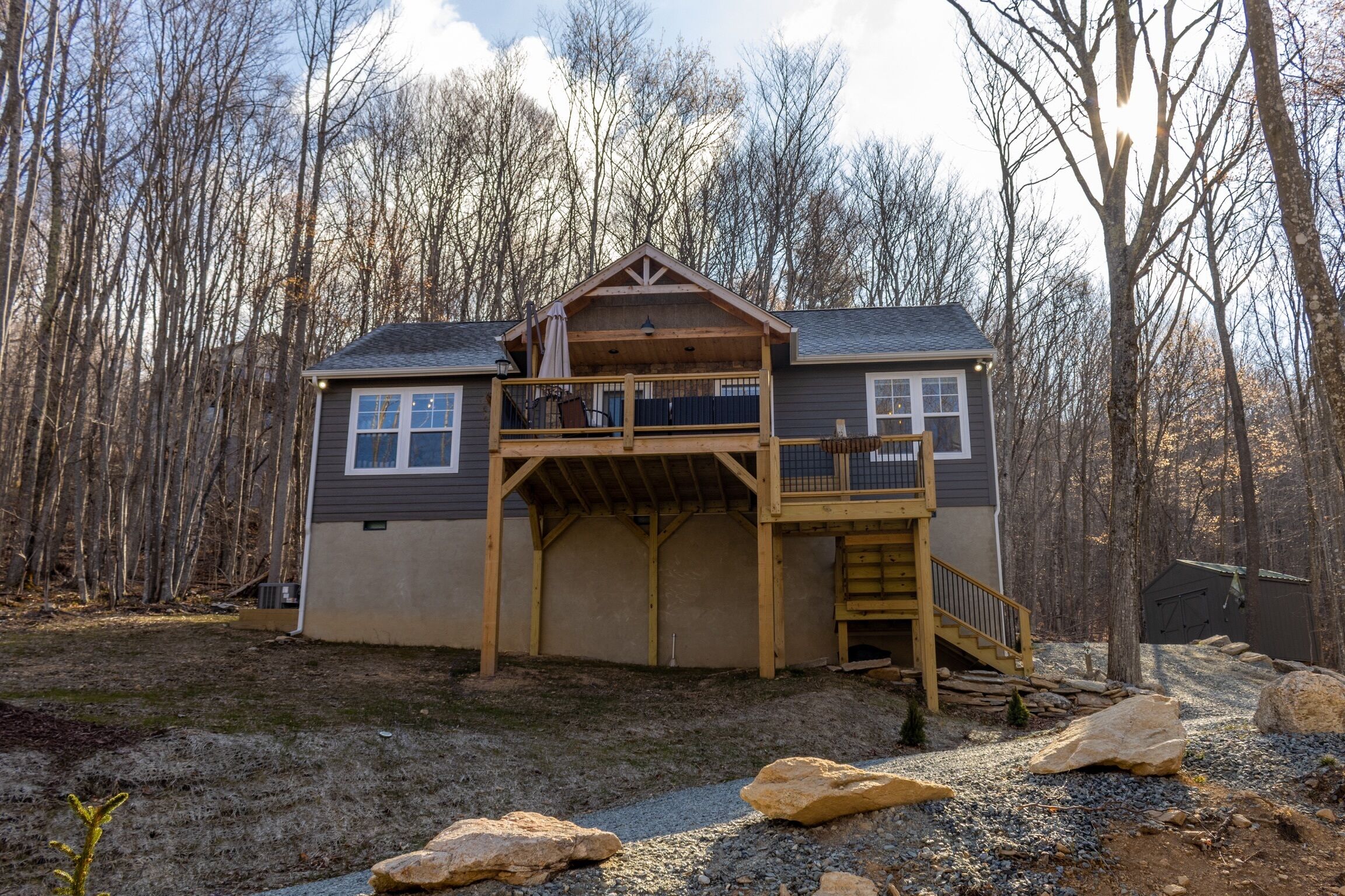 A two-story house with a wooden deck, a covered porch, and a staircase leading to the upper level.