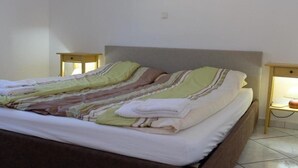 Ein ordentlich bezogenes Bett mit gestreifter Bettwäsche, zwei Nachttische mit Lampen und eine schlichte Wand.
