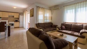 Una sala de estar con un conjunto de sofá, una mesa de centro y una zona de cocina con armarios y electrodomésticos.