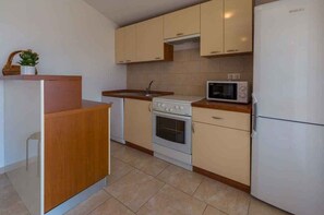 Compact kitchen with oven, sink, and refrigerator, featuring light cabinetry and a countertop.