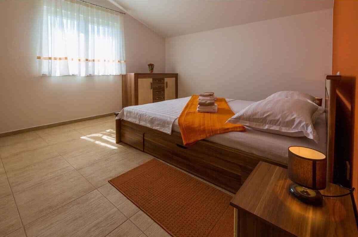 Un lit simple avec une tête de lit en bois, une table de chevet avec une lampe et une fenêtre ornée de rideaux légers.