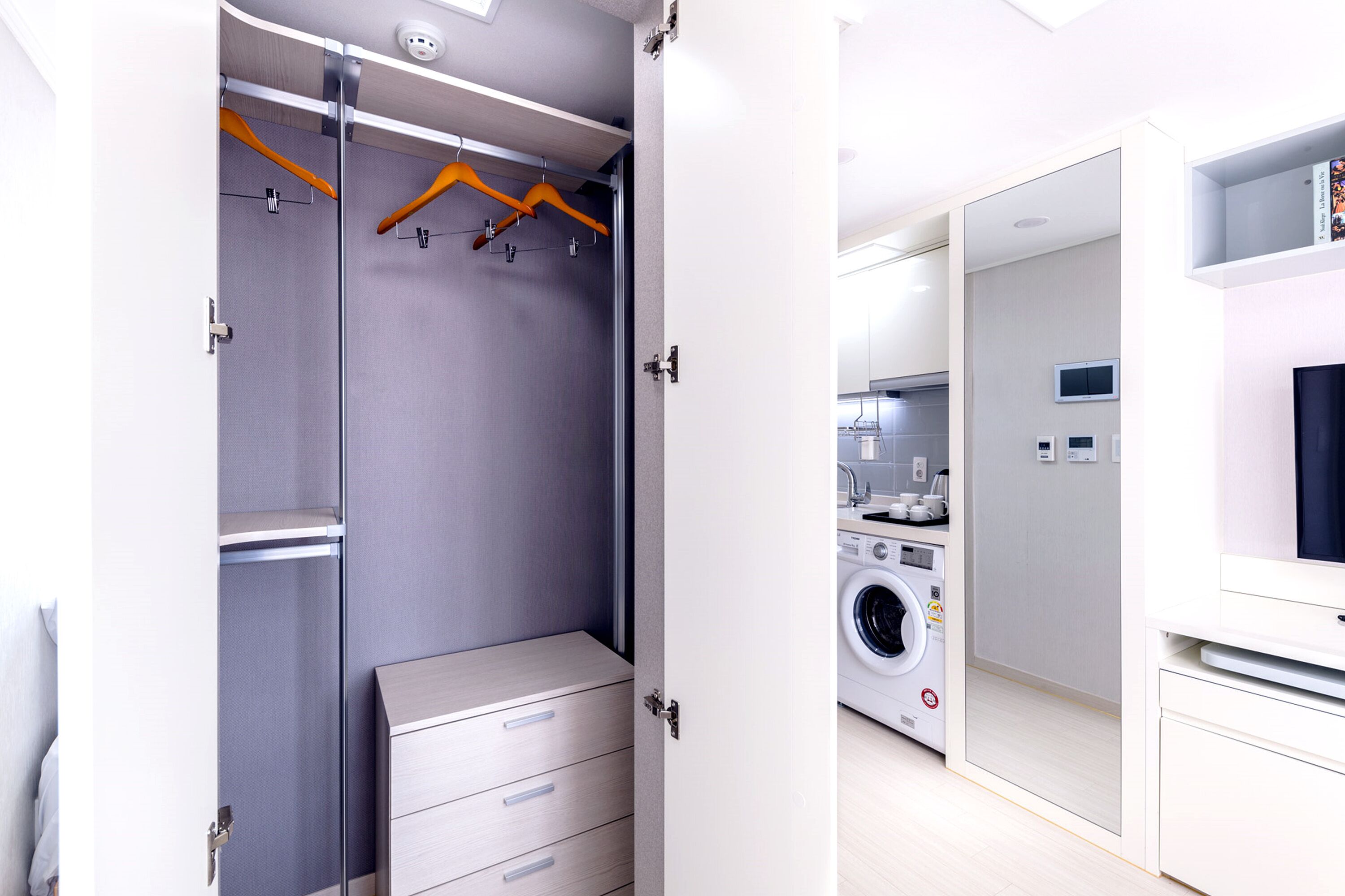 Ein modernes, helles Zimmer mit einem grauen Wäscheschrank, hölzernen Kleiderbügeln und einer Waschmaschine.