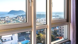 Une vue à travers une fenêtre à carreaux multiples, offrant notamment un panorama sur un paysage urbain côtier avec des bâtiments et un pont.