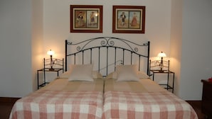 Una cama doble con una colcha a cuadros, dos mesitas de noche con lámparas y dos cuadros enmarcados en la pared.