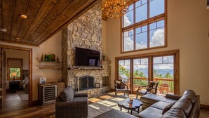 Amplia sala de estar con chimenea de piedra, sofás de cuero y grandes ventanales con vistas al exterior.