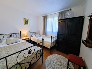 Quarto com duas camas de solteiro, um guarda-roupa de madeira, uma mesa redonda pequena e uma cadeira.