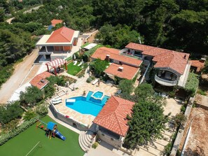 Vista aérea de uma propriedade residencial com piscina, várias casas e quadra de tênis.
