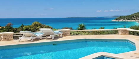 Una piscina con sillones de descanso y vistas al mar.