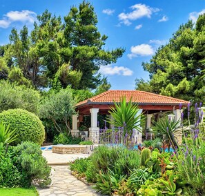 A gazebo with a tiled roof surrounded by lush greenery and a stone pathway. - Apartment "Fantasy" with 2 bed rooms, terraces, swimming pool, jacuzzy. Sea view (Poplat Vela Luka)