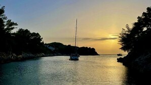 Een zeilboot op kalm water, met een zonsondergang op de achtergrond.