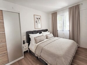 Et soveværelse med seng, et natbord, et billede i ramme på væggen og et vindue med gardiner.