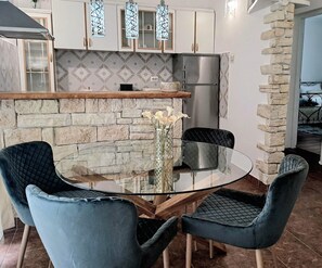 Een moderne keuken met een stenen muur, een roestvrijstalen koelkast en een glazen eettafel met twee stoelen.