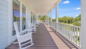 A covered porch with white rocking chairs and a view of a lush green landscape.