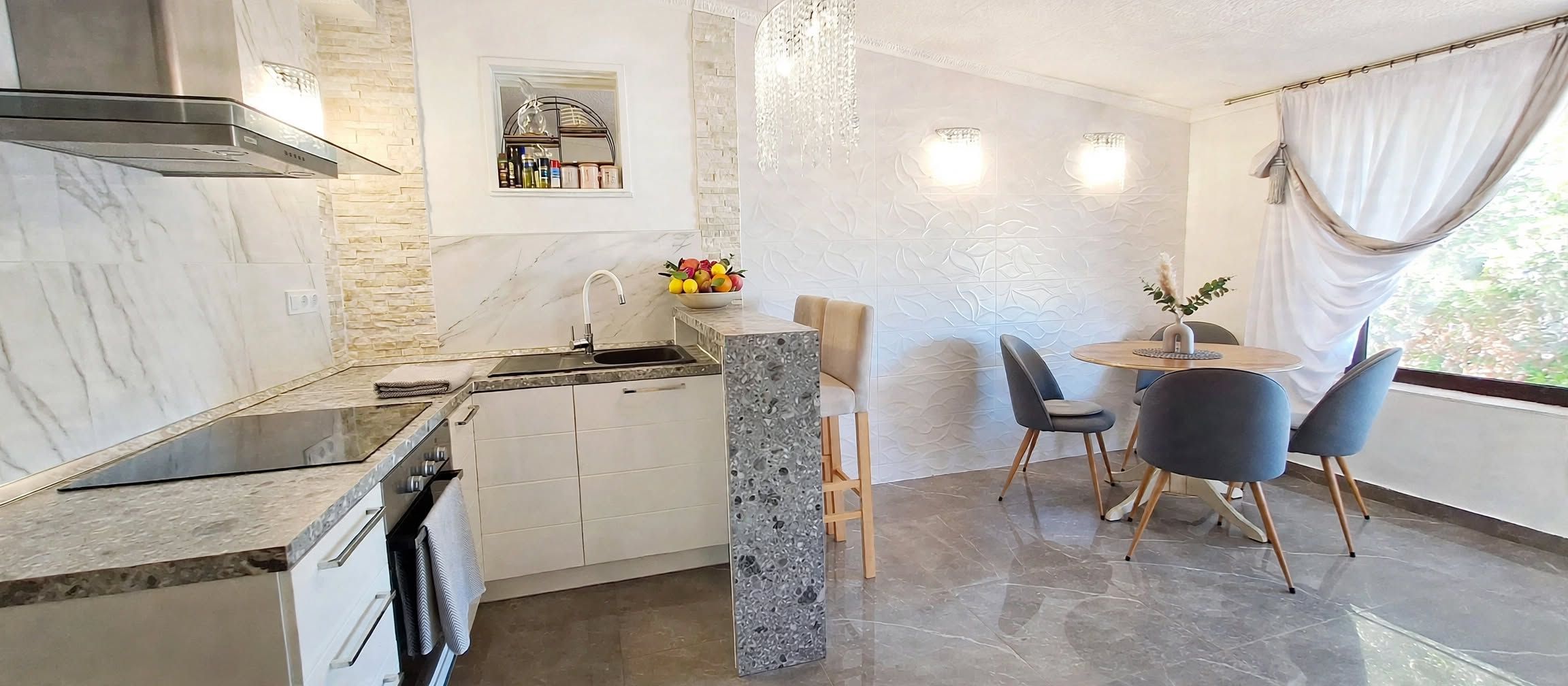 A modern kitchen with a built-in stove, a sink, and a dining area with a round table and chairs.