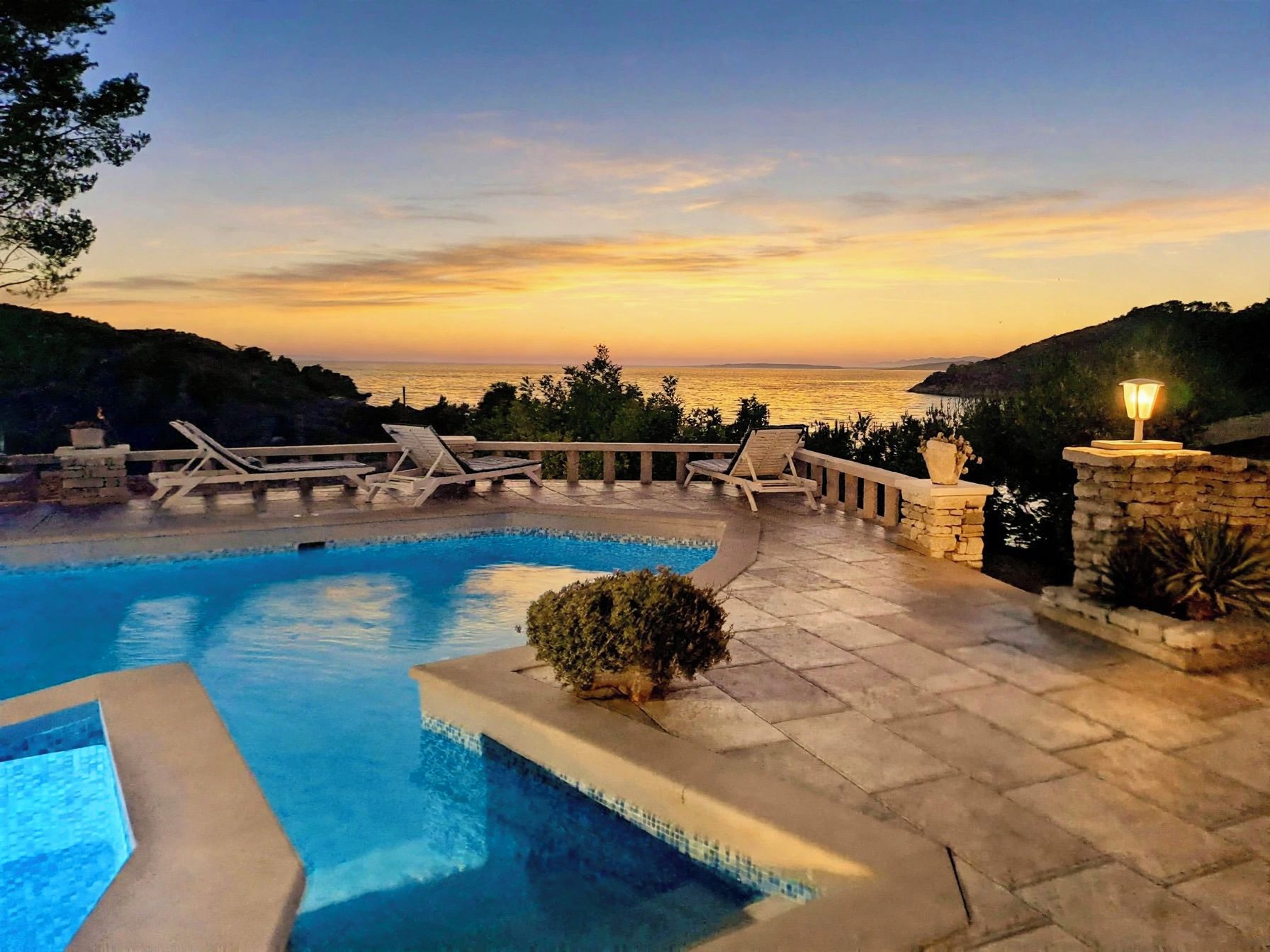 A swimming pool with lounge chairs and a view of the sea at sunset.