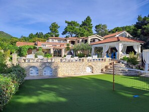 En stenvilla med pool, udendørs møbler og tennisbane.