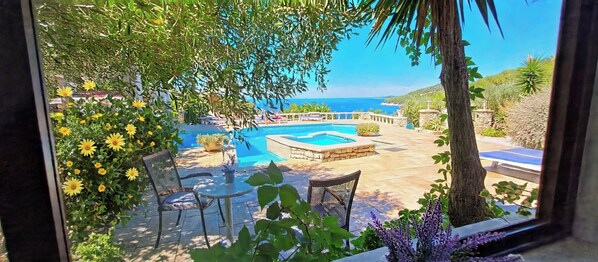 A pool area with a view of the sea, outdoor seating, and a stone pathway.