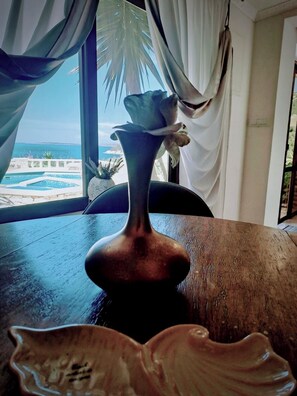 A vase with a flower on a wooden table by a window with a view of a pool and palm trees. - Apartment "Romantic" - luxurious (Poplat Vela Luka)