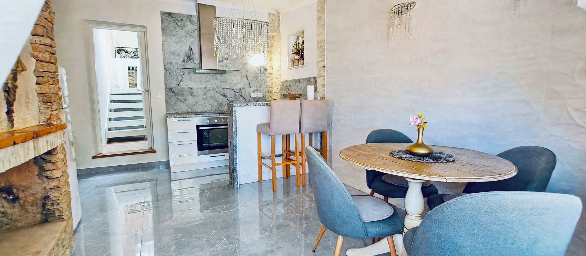 A modern kitchen with a marble countertop, a built-in oven, and a hanging light fixture.