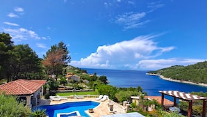 Zona de piscina con vistas al mar, rodeada de vegetación y edificios.