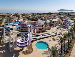 A water park with multiple slides and a pool, surrounded by buildings and palm trees. - Caldera Beach (Gerani)