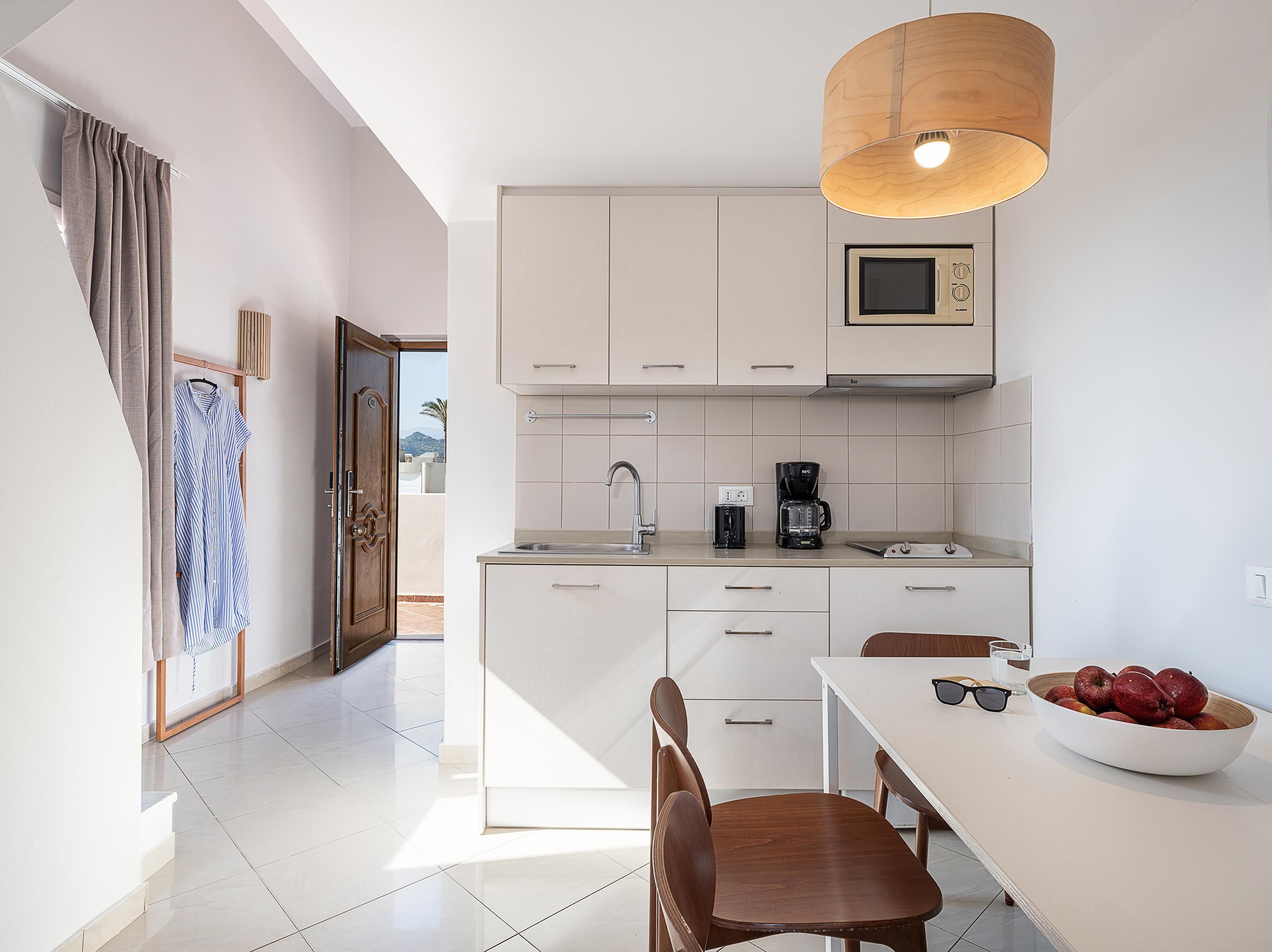 Una cocina moderna con armarios blancos, una mesa de comedor de madera y un bol de fruta.