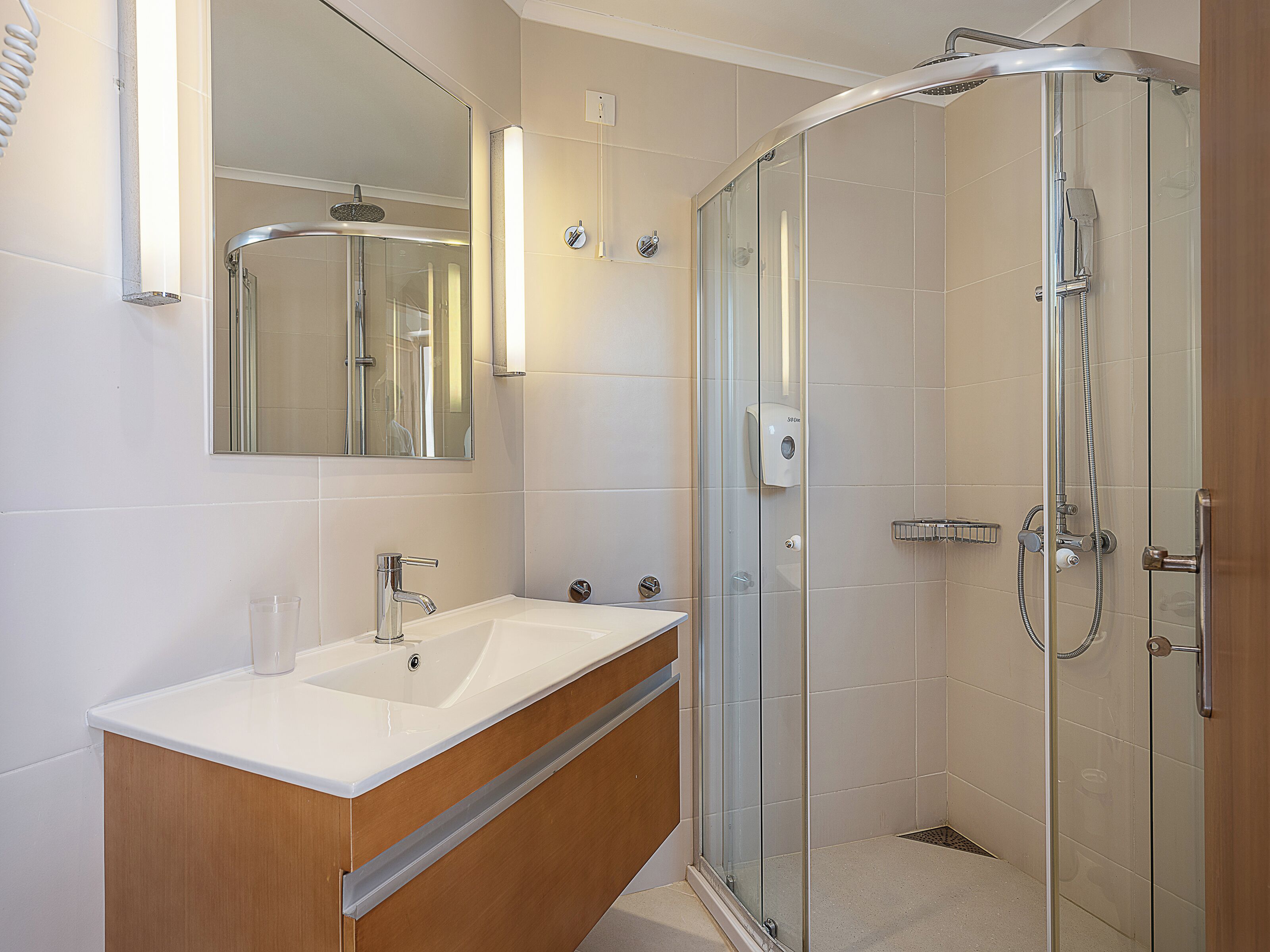 A modern bathroom with a glass-enclosed shower, a wooden vanity, and a large mirror.