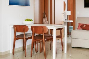 A dining area with a white table and four wooden chairs, a bowl of fruit, and a polka-dotted bag on the table.