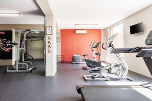 Et fitnesscenter med forskellig træningsudstyr, heriblandt løbebånd og styrkemaskiner, samt en rød accentvæg.