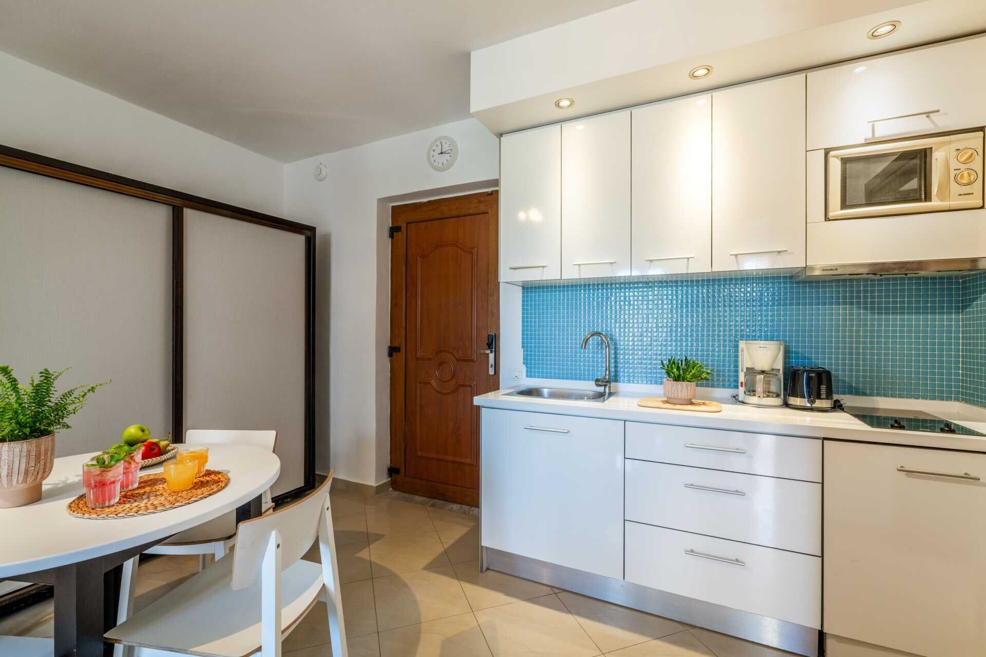 A modern kitchen with white cabinets, a blue tiled backsplash, and a coffee maker on the counter.