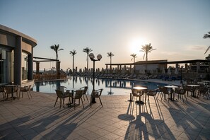 A poolside area with lounge chairs and tables, palm trees, and a clear sky. - Caldera Beach (Gerani)