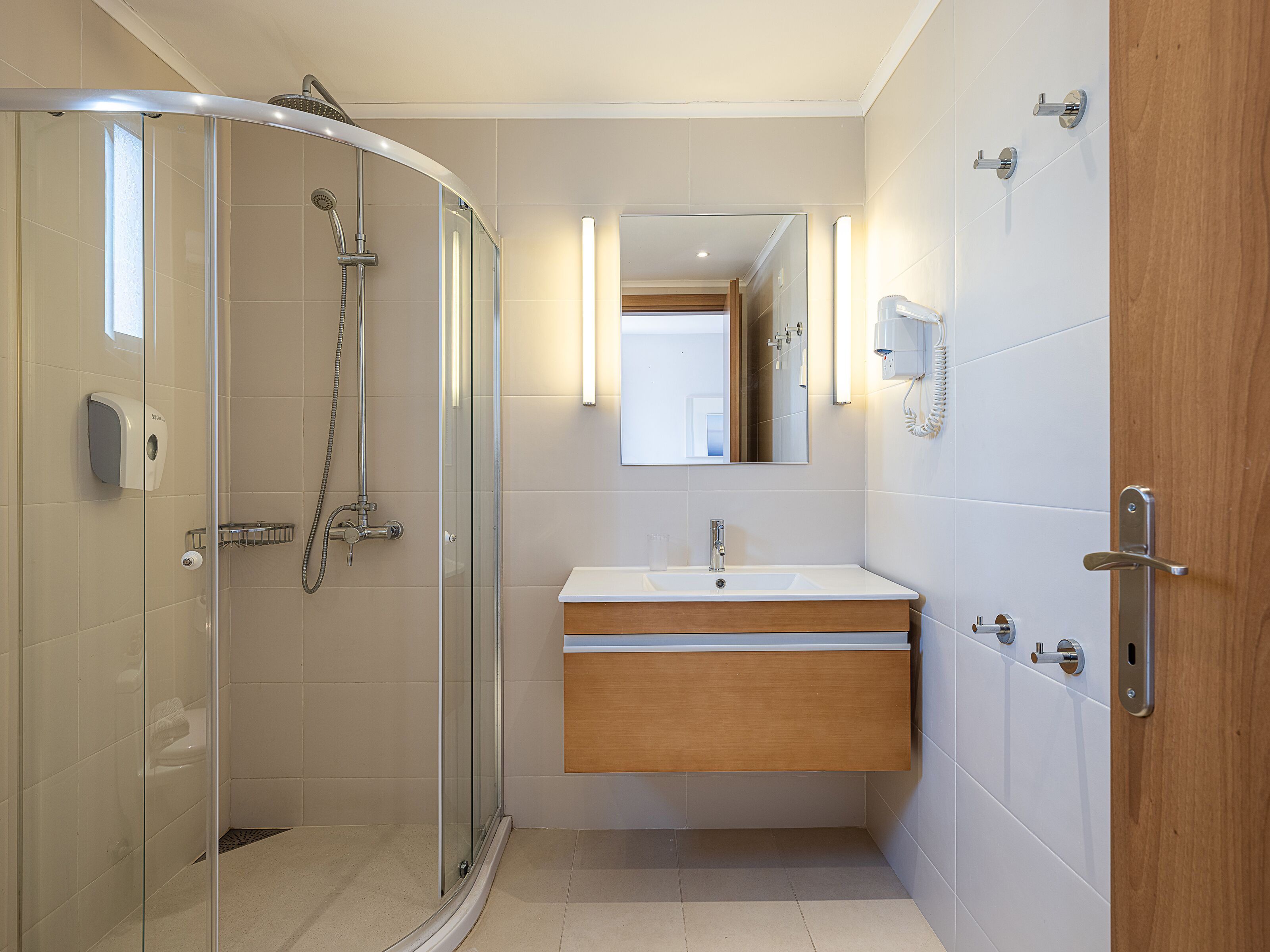 Un baño moderno con cabina de ducha de vidrio, tocador de madera y espejo sobre el lavabo.