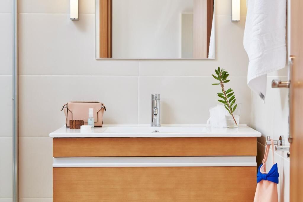 Een badkamer met een wit wastafel, houten wastafelmeubel en een spiegel erboven.