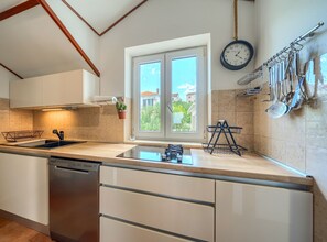 A modern kitchen with a sink, dishwasher, and a window with a view of houses. - Apartments Vrandecic (Postira)