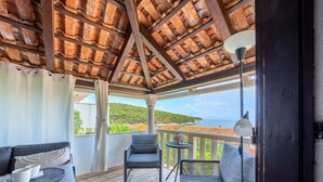 A covered outdoor seating area with a view of the sea, a table with a vase, and a chair. - Apartments Vrandecic (Postira)