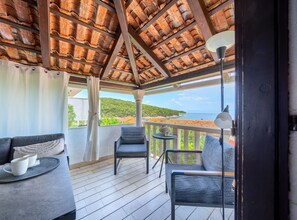 A covered outdoor seating area with a view of the sea, a table with a vase, and a chair. - Apartments Vrandecic (Postira)