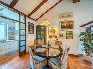 A dining area with a round table, wicker chairs, and a hanging light fixture. - Apartments Vrandecic (Postira)