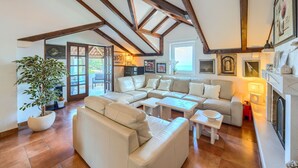 A spacious living room with a high ceiling, exposed wooden beams, a large sofa set, a dining table, and a fireplace. - Apartments Vrandecic (Postira)