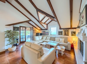 A spacious living room with a high ceiling, exposed wooden beams, a large sofa set, a dining table, and a fireplace. - Apartments Vrandecic (Postira)