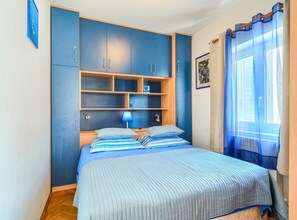 A bedroom with a bed, a wardrobe, a shelf unit, a lamp, and a window with curtains. - Apartments Vrandecic (Postira)